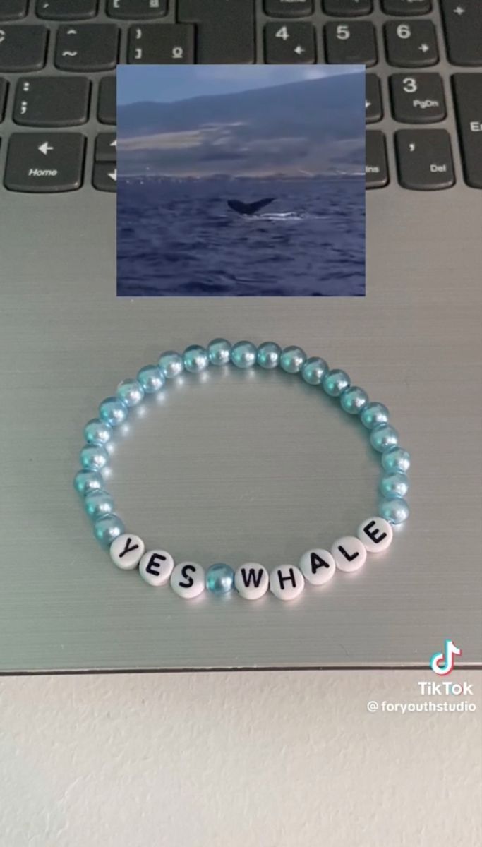 a beaded bracelet with the words yes whale on it sits next to a laptop keyboard