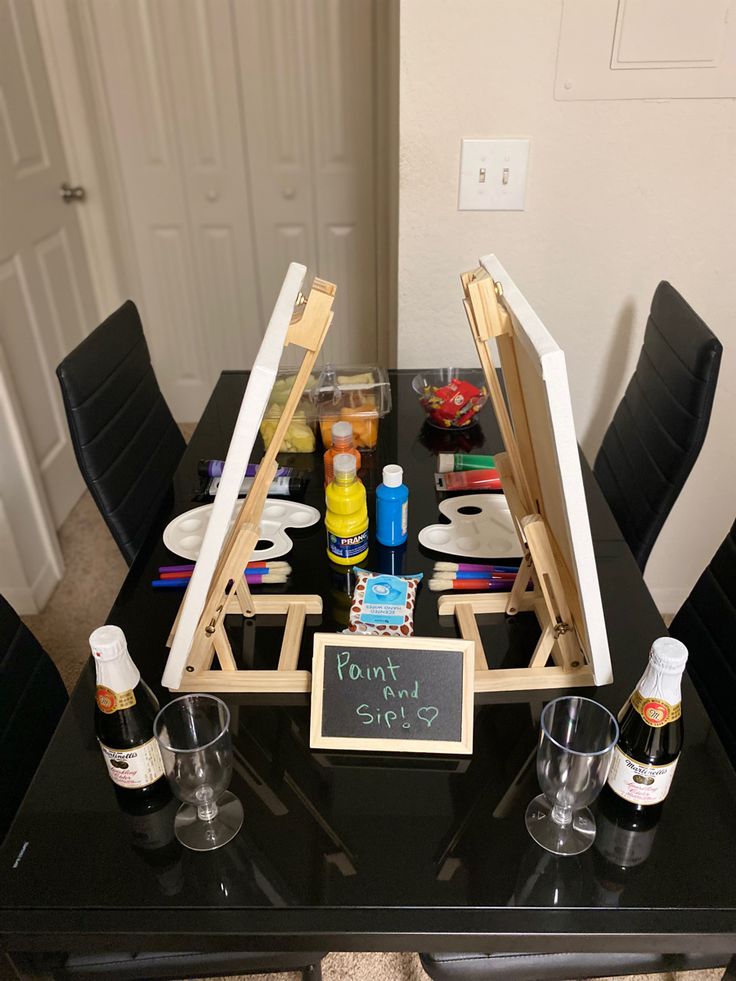 an easel is set up on top of a table with wine glasses and other items