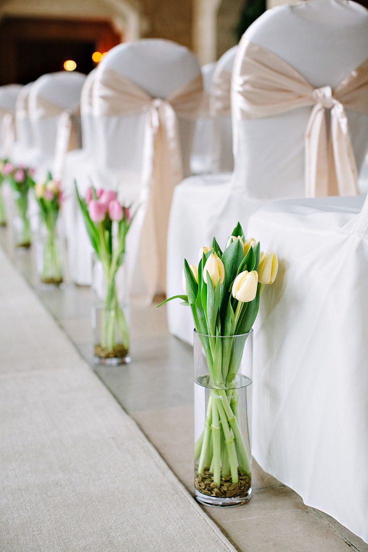 flowers in vases are lined up on the side of a row of white chairs