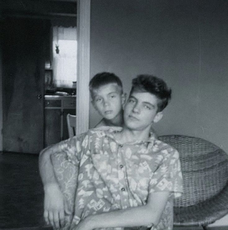 two young men are sitting on a wicker chair and one is holding his arm around the other