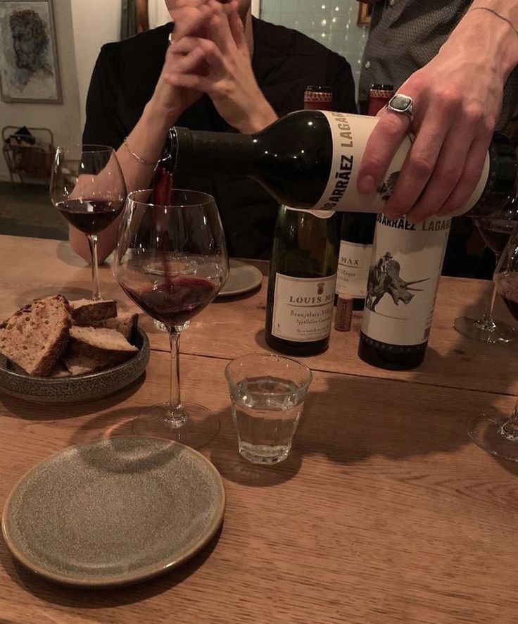 a person pouring wine into a glass at a table with food and glasses on it