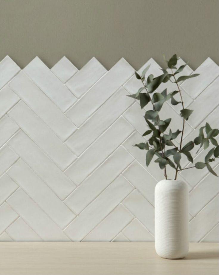 a plant in a white vase sitting on a table next to a wall with chevron tiles