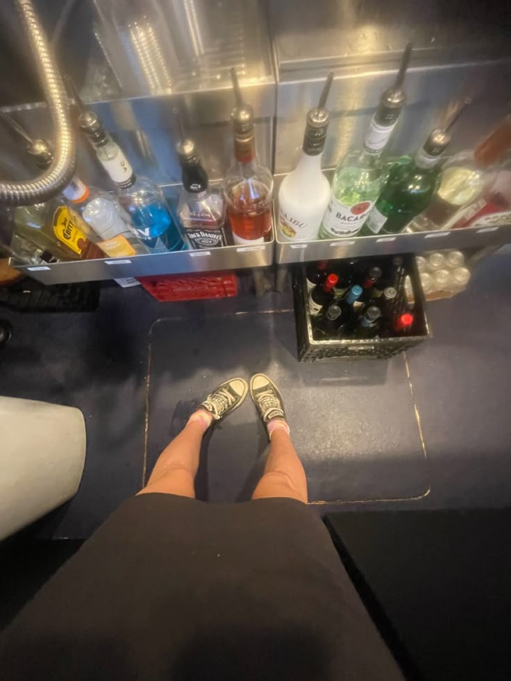 the person is sitting in front of an open refrigerator filled with bottles and liquors