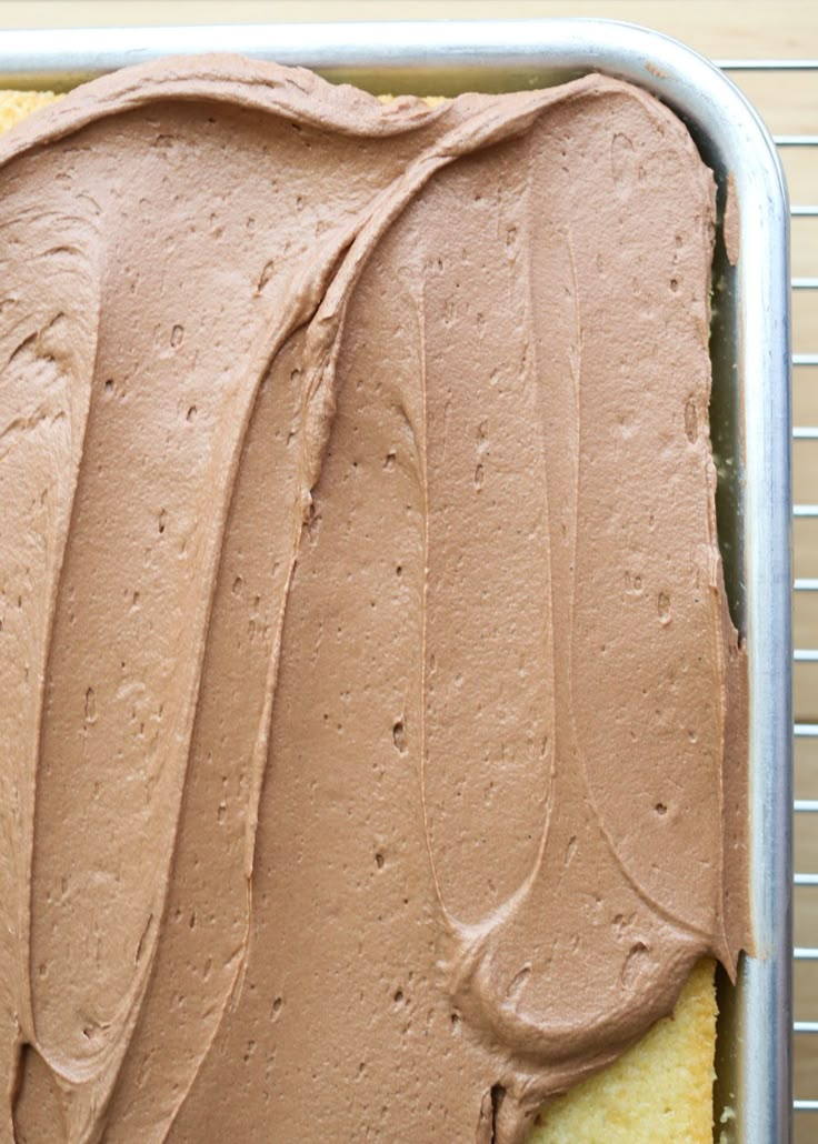 a cake with chocolate frosting in a metal pan on a cooling rack, ready to be eaten