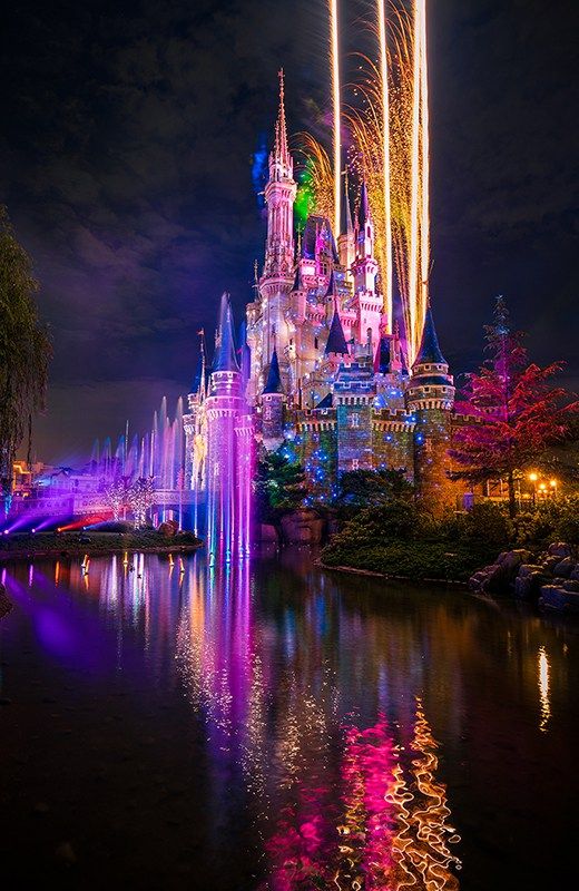 the castle is lit up at night with colorful lights and fireworks in the sky above it