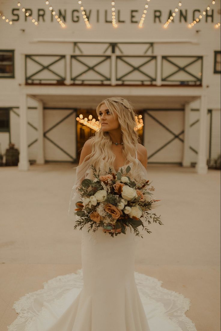 a woman in a wedding dress holding a bouquet and looking off into the distance with lights behind her