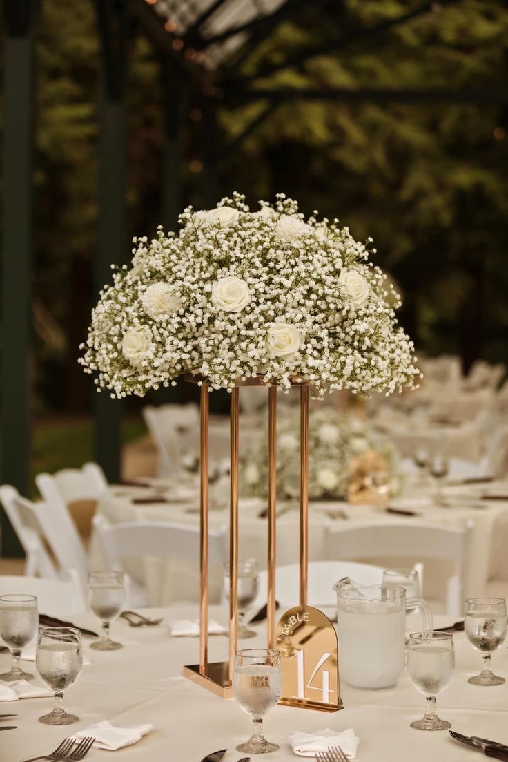 the table is set with silverware and white flowers in vases on gold stands