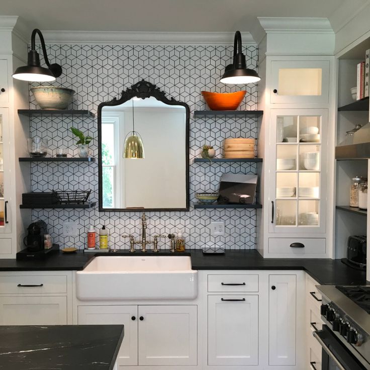 a kitchen with white cabinets and black counter tops, along with a large mirror above the sink