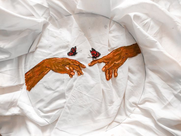 two painted hands touching each other with butterflies on top of the white sheeted surface