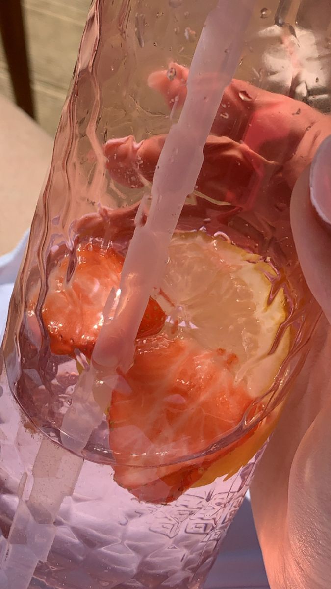 a person holding a glass filled with water and orange slices