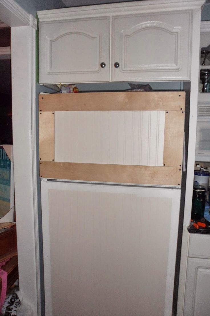 a kitchen with white cupboards and an unfinished shelf on the wall above the refrigerator