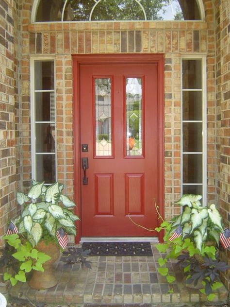 a red door with two planters in front of it and an arched glass window