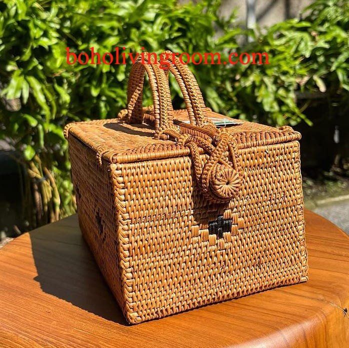 a brown wicker purse sitting on top of a wooden table next to some bushes