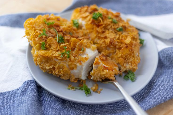 a white plate topped with food on top of a blue and white table cloth next to a fork