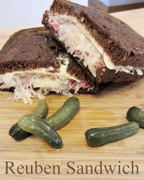 a sandwich cut in half with pickles on a cutting board next to it that says reuben sandwich