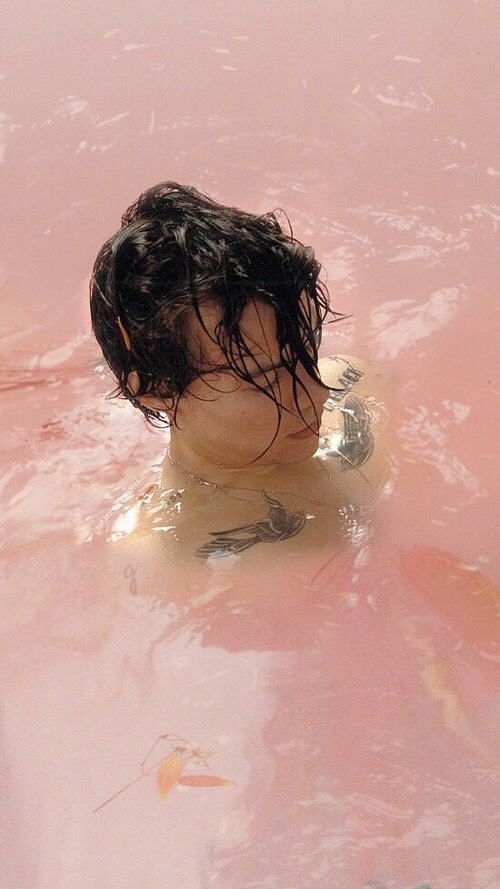 a young boy swimming in a pink pool with no shirt on and his head sticking out