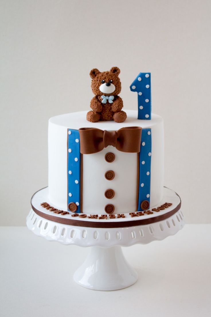 a birthday cake with a teddy bear on top and the number one decorated in fondant