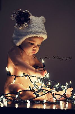 a baby is sitting on the floor with christmas lights all around her and wearing a hat