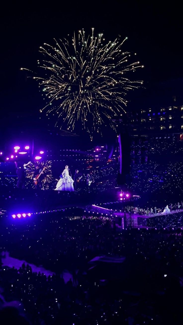 fireworks are lit up in the night sky above a large crowd at an outdoor concert