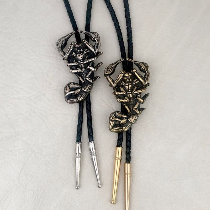 "Original scorpion design was hand carved, then cast in the Heliotrope studio in Tucson, AZ. Cast in solid brass (gold tone), or white bronze (silver tone). Cord is machine braided black or tan leather. At checkout, please choose the desired cord length: 36\"----- Recommended for people under 6' tall. 42\"----- Recommended for people 6' tall or taller. Scorpion measures 2.4\" tall x 1.5\" wide. PLEASE NOTE: final two photos (AND the video) show a comparison between the LARGE SCORPION BOLO TIE (t Black Engraved Western Jewelry, Artisan Hand-tooled Jewelry For Rodeo, Vintage Black Jewelry For Western-themed Events, Western Engraved Jewelry For Rodeo, Black Concho Jewelry For Western-themed Events, Black Southwestern Jewelry For Rodeo, Western Style Engraved Jewelry For Rodeo, Southwestern Black Jewelry For Rodeo, Western Black Jewelry For Rodeo