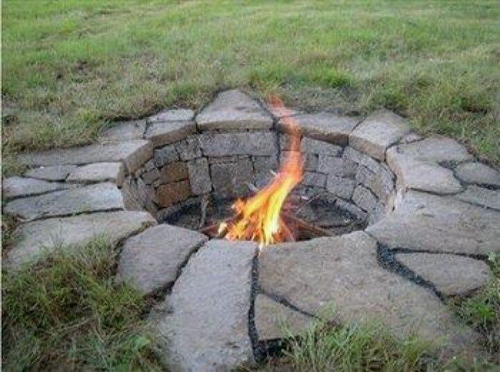 an open fire pit in the middle of a field with grass and rocks around it