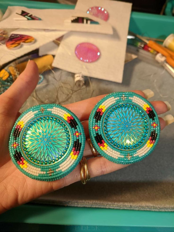 a person holding two colorful beaded earrings in their hand next to some other items