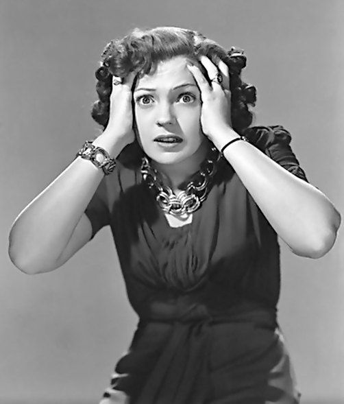 a woman holding her hands to her head while looking at the camera with an intense look on her face