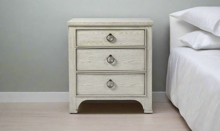 a white nightstand with two drawers next to a bed