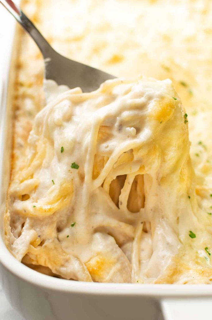 a casserole dish with chicken and cheese being scooped from the casserole