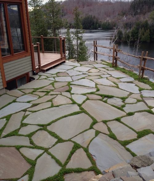 a stone walkway with grass growing on it next to a house and water in the background