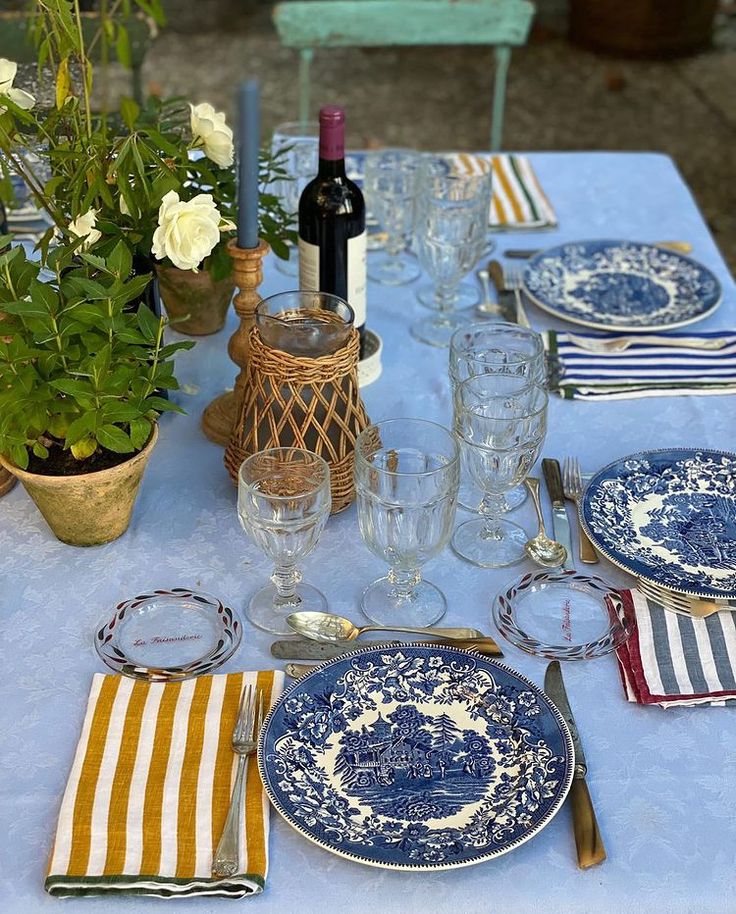 the table is set with blue and white plates, silverware, wine glasses, and flowers