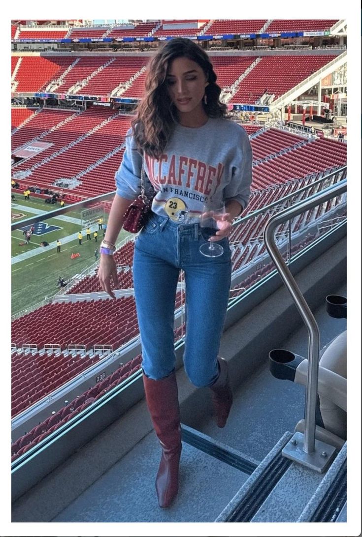 a woman in jeans and boots is standing on the bleachers at a football stadium