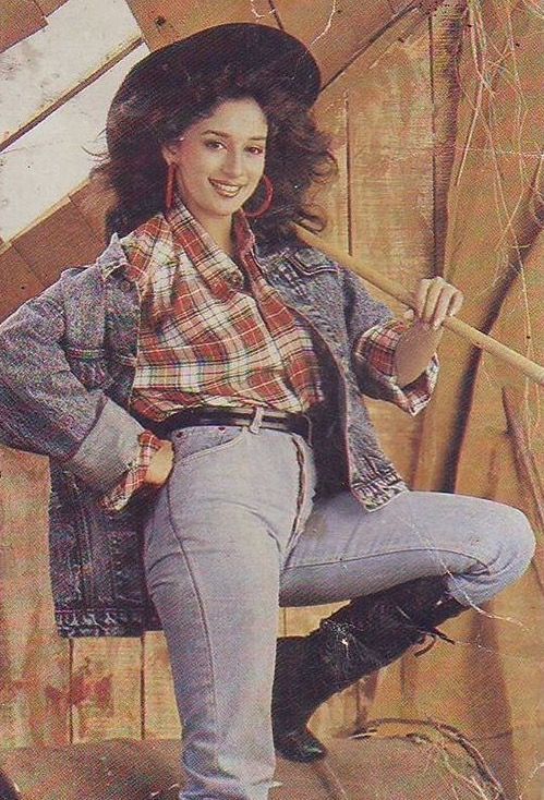 a woman sitting on top of a wooden bench wearing jeans and a plaid shirt holding an umbrella