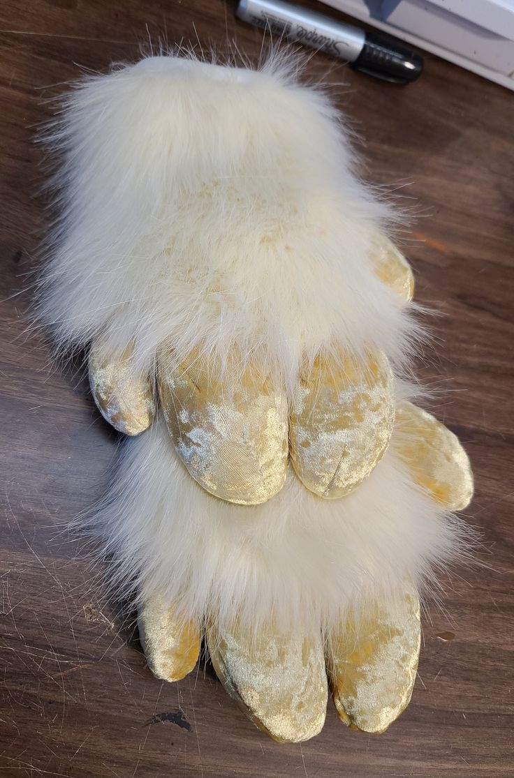 a yellow stuffed animal with white fur on it's back legs and feet sitting on a wooden surface