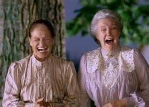 two women laughing and standing next to each other in front of a tree with their mouths open