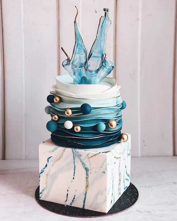 a multi layer cake with blue frosting and gold beads on the top, sitting on a marble block