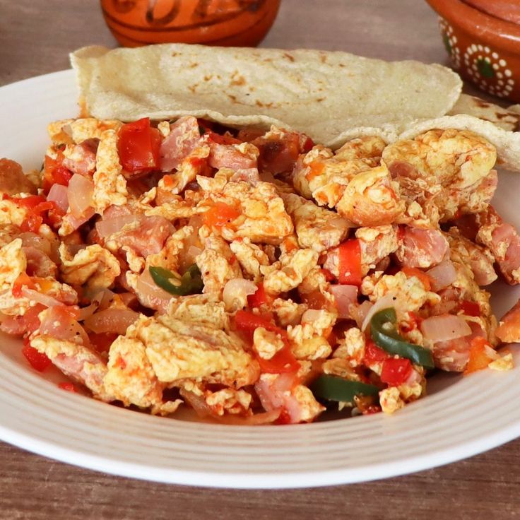 a white plate topped with an egg and meat dish next to a tortilla