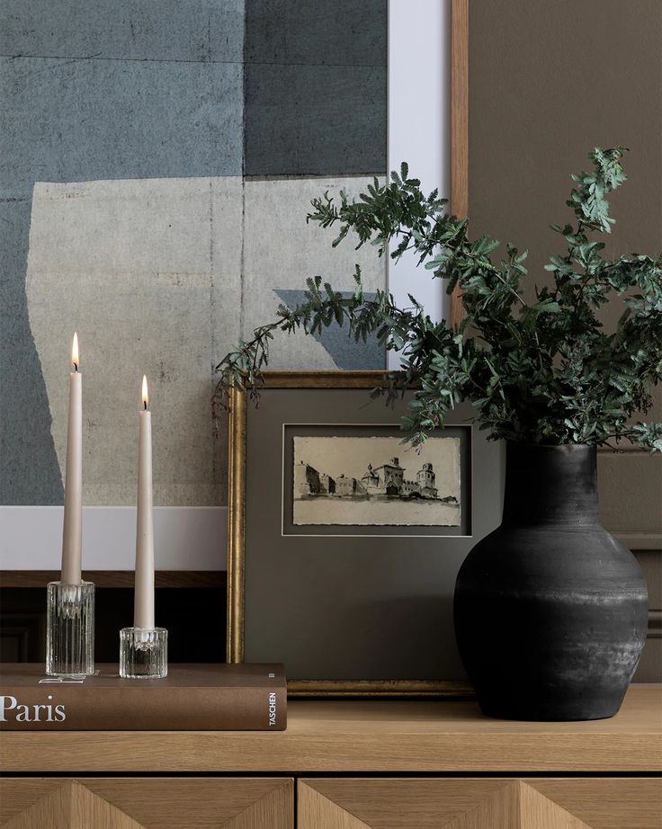 a black vase sitting on top of a wooden table next to two candles and a book