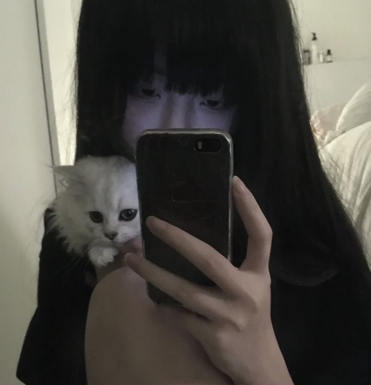 a woman taking a selfie with her cell phone and a cat on her shoulder