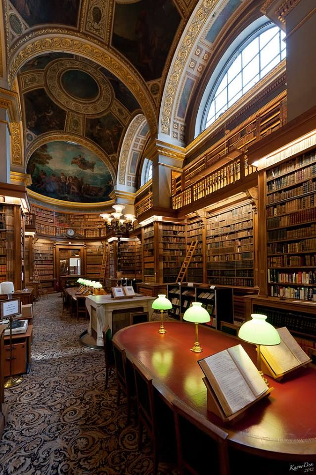 an old library with many bookshelves and two lamps on the tables in front of them