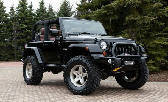 a black jeep is parked in front of some trees and brick pavers on a driveway