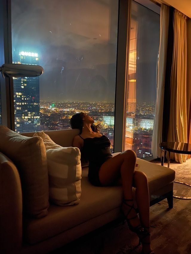 a woman sitting on top of a couch in front of a large window at night