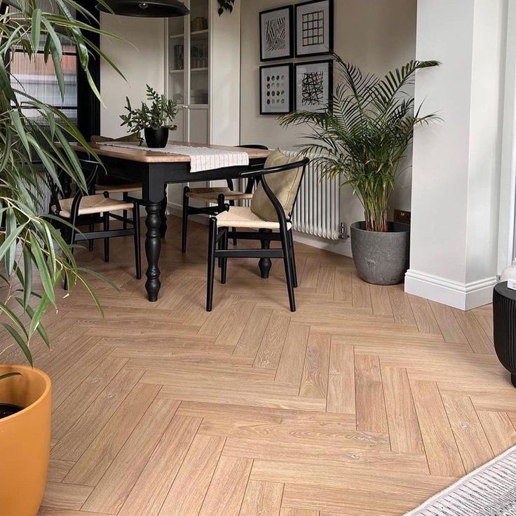 a dining room table and chairs with potted plants on the floor next to it