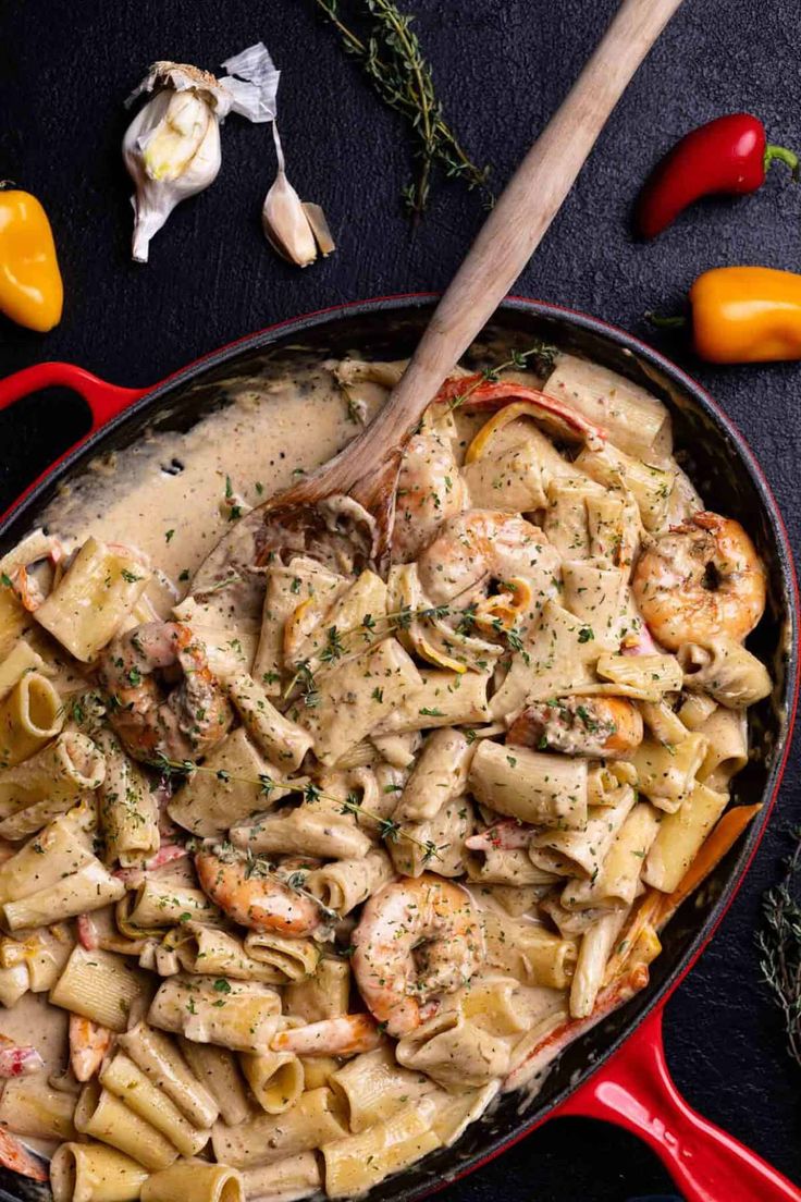 a skillet filled with pasta, shrimp and sauce on top of a black table