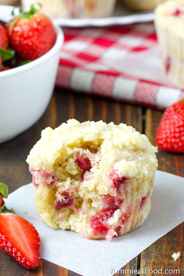 a muffin with strawberries on the side and a bowl of strawberries in the background