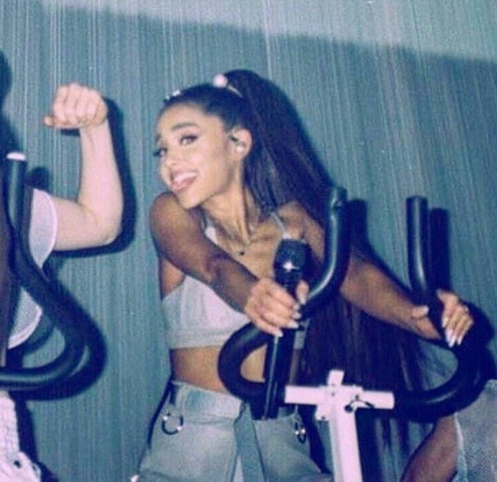 two women on exercise bikes in a gym with one woman smiling and the other standing up