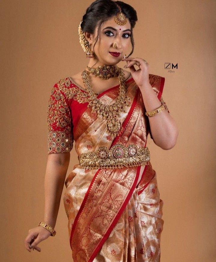 a woman in a red and gold sari with jewelry on her neck, holding a magnifying glass up to her nose