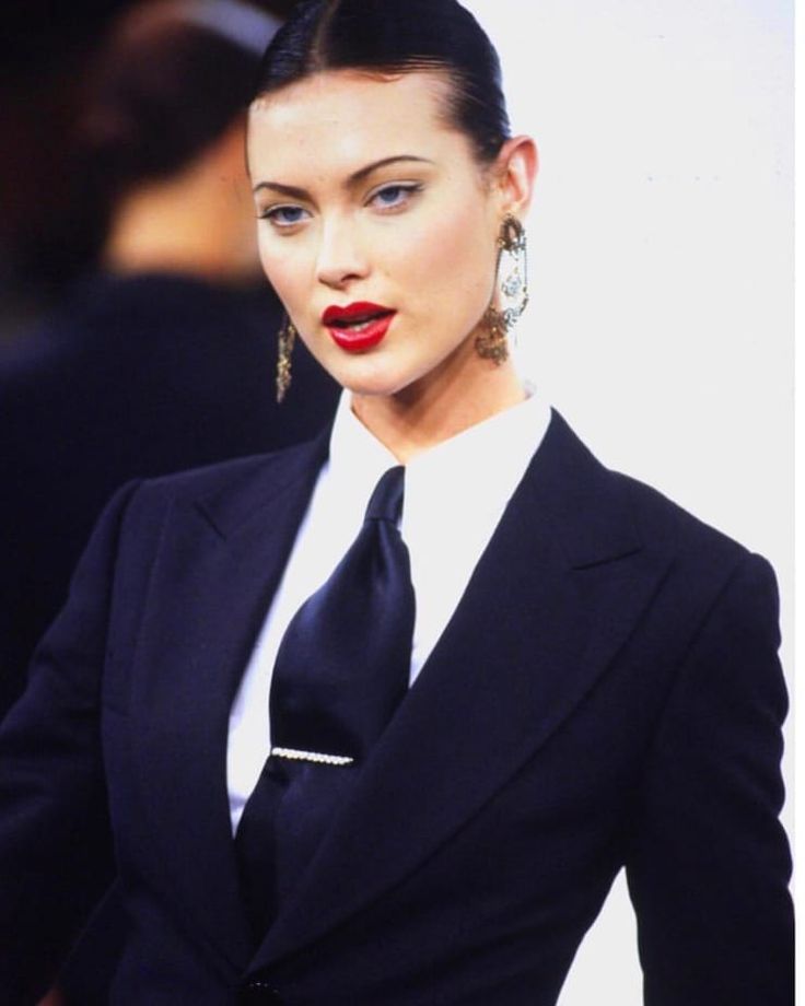 a woman in a black suit and white shirt with red lipstick on her lips is looking off to the side