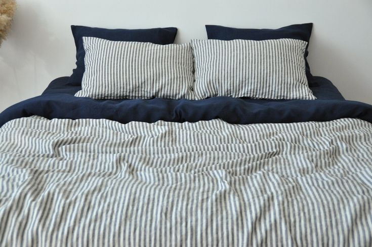 an unmade bed with blue and white striped sheets, pillows and a teddy bear