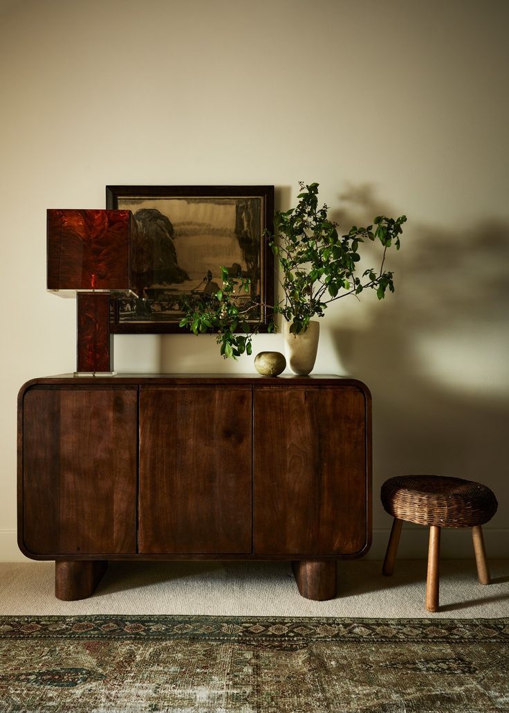 a wooden cabinet sitting next to a potted plant on top of a table in front of a mirror